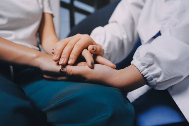 Doktor umut veriyor. Genç kadın hekimin avuçlarında elini tutan yaşlı bayanın gülümsemesini yakından çek. Beyaz önlüklü kadın bakıcı yaşlı insanı cesaretlendiriyor.