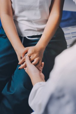 Doktor umut veriyor. Genç kadın hekimin avuçlarında elini tutan yaşlı bayanın gülümsemesini yakından çek. Beyaz önlüklü kadın bakıcı yaşlı insanı cesaretlendiriyor.