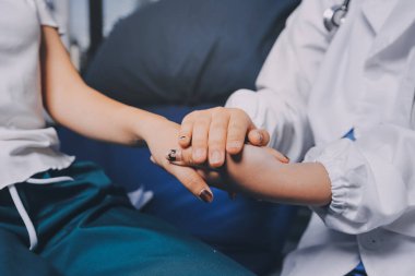 Doktor umut veriyor. Genç kadın hekimin avuçlarında elini tutan yaşlı bayanın gülümsemesini yakından çek. Beyaz önlüklü kadın bakıcı yaşlı insanı cesaretlendiriyor.