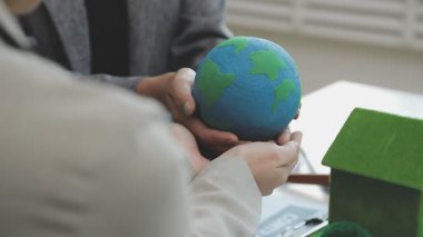 Masasında bir model ev ve rüzgar türbini olan sürdürülebilir ve çevre dostu gayrimenkul projelerini tartışan profesyoneller.