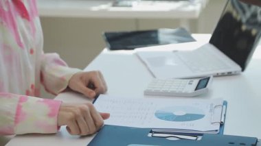 İki finans muhasebecisi dizüstü bilgisayardaki iş tablolarını analiz ediyor, ofis masasında oturuyor, kağıt belgelerine bakıyor, veri tabanlarıyla çalışan hesap makinesi kullanıyor, üstün tabloları kontrol ediyor.