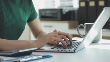 İki finans muhasebecisi dizüstü bilgisayardaki iş tablolarını analiz ediyor, ofis masasında oturuyor, kağıt belgelerine bakıyor, veri tabanlarıyla çalışan hesap makinesi kullanıyor, üstün tabloları kontrol ediyor.