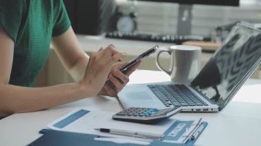 İki finans muhasebecisi dizüstü bilgisayardaki iş tablolarını analiz ediyor, ofis masasında oturuyor, kağıt belgelerine bakıyor, veri tabanlarıyla çalışan hesap makinesi kullanıyor, üstün tabloları kontrol ediyor.