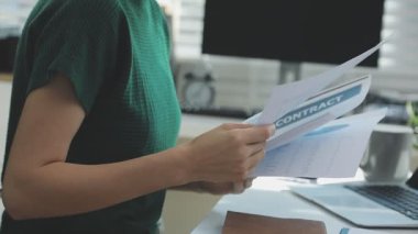 İki finans muhasebecisi dizüstü bilgisayardaki iş tablolarını analiz ediyor, ofis masasında oturuyor, kağıt belgelerine bakıyor, veri tabanlarıyla çalışan hesap makinesi kullanıyor, üstün tabloları kontrol ediyor.