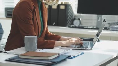 İki finans muhasebecisi dizüstü bilgisayardaki iş tablolarını analiz ediyor, ofis masasında oturuyor, kağıt belgelerine bakıyor, veri tabanlarıyla çalışan hesap makinesi kullanıyor, üstün tabloları kontrol ediyor.