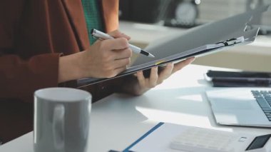 İki finans muhasebecisi dizüstü bilgisayardaki iş tablolarını analiz ediyor, ofis masasında oturuyor, kağıt belgelerine bakıyor, veri tabanlarıyla çalışan hesap makinesi kullanıyor, üstün tabloları kontrol ediyor.