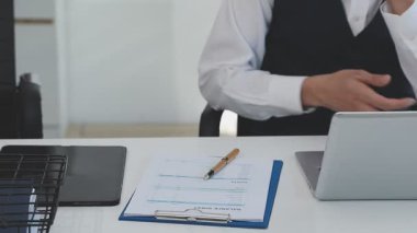 İki finans muhasebecisi dizüstü bilgisayardaki iş tablolarını analiz ediyor, ofis masasında oturuyor, kağıt belgelerine bakıyor, veri tabanlarıyla çalışan hesap makinesi kullanıyor, üstün tabloları kontrol ediyor.