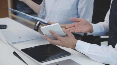 İki finans muhasebecisi dizüstü bilgisayardaki iş tablolarını analiz ediyor, ofis masasında oturuyor, kağıt belgelerine bakıyor, veri tabanlarıyla çalışan hesap makinesi kullanıyor, üstün tabloları kontrol ediyor.