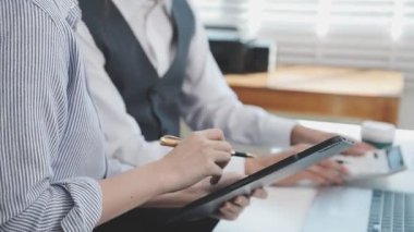 İki finans muhasebecisi dizüstü bilgisayardaki iş tablolarını analiz ediyor, ofis masasında oturuyor, kağıt belgelerine bakıyor, veri tabanlarıyla çalışan hesap makinesi kullanıyor, üstün tabloları kontrol ediyor.