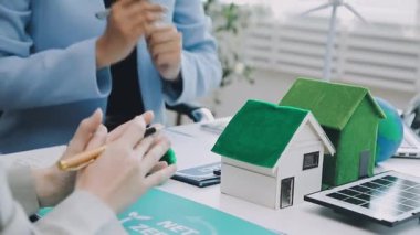 Masasında bir model ev ve rüzgar türbini olan sürdürülebilir ve çevre dostu gayrimenkul projelerini tartışan profesyoneller.