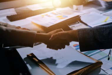 Girişimcilerin işbirliği anlaşması modern bir ofiste el sıkışıyor ve masadaki finansal kağıt grafiği.