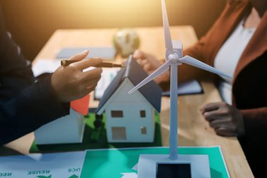 Ekip toplantısında, ESG konu sunumu için dizüstü bilgisayar kullanan Asyalı kadın, çok ırklı iş adamlarından oluşan genç bir gruba liderlik ediyor. Sürdürülebilir iş uygulaması, insanlar ev konseptinde çalışıyor