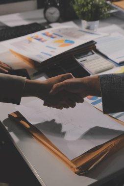 Girişimcilerin işbirliği anlaşması modern bir ofiste el sıkışıyor ve masadaki finansal kağıt grafiği.