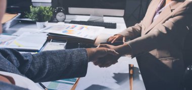 Girişimcilerin işbirliği anlaşması modern bir ofiste el sıkışıyor ve masadaki finansal kağıt grafiği.