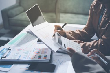 İş arkadaşları, modern bir ofis ortamında yapılan önemli bir toplantıda strateji ve piyasa performansı hakkında tartışırken finansal tablolar ve raporları analiz ediyorlar.