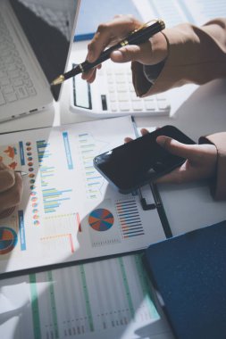 İş arkadaşları, modern bir ofis ortamında yapılan önemli bir toplantıda strateji ve piyasa performansı hakkında tartışırken finansal tablolar ve raporları analiz ediyorlar.