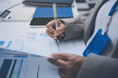 İş arkadaşları, modern bir ofis ortamında yapılan önemli bir toplantıda strateji ve piyasa performansı hakkında tartışırken finansal tablolar ve raporları analiz ediyorlar.