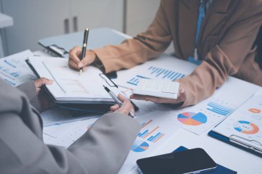 İş arkadaşları, modern bir ofis ortamında yapılan önemli bir toplantıda strateji ve piyasa performansı hakkında tartışırken finansal tablolar ve raporları analiz ediyorlar.