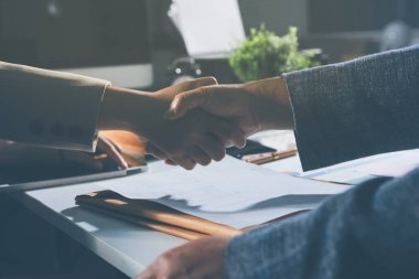 Girişimcilerin işbirliği anlaşması modern bir ofiste el sıkışıyor ve masadaki finansal kağıt grafiği.