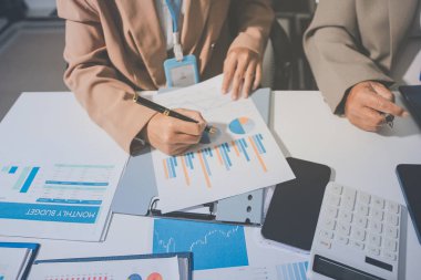 İş arkadaşları, modern bir ofis ortamında yapılan önemli bir toplantıda strateji ve piyasa performansı hakkında tartışırken finansal tablolar ve raporları analiz ediyorlar.