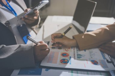 İş arkadaşları, modern bir ofis ortamında yapılan önemli bir toplantıda strateji ve piyasa performansı hakkında tartışırken finansal tablolar ve raporları analiz ediyorlar.