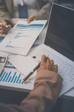 İş arkadaşları, modern bir ofis ortamında yapılan önemli bir toplantıda strateji ve piyasa performansı hakkında tartışırken finansal tablolar ve raporları analiz ediyorlar.