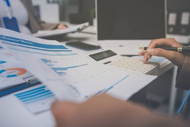 İş arkadaşları, modern bir ofis ortamında yapılan önemli bir toplantıda strateji ve piyasa performansı hakkında tartışırken finansal tablolar ve raporları analiz ediyorlar.