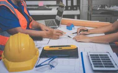 Mühendis ve mimar, hareketli bir şantiyede planlar ve inşaat planlarını birlikte gözden geçiriyorlar.