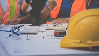 Mühendis ve mimar, hareketli bir şantiyede planlar ve inşaat planlarını birlikte gözden geçiriyorlar.