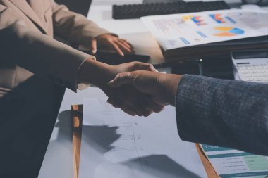 Girişimcilerin işbirliği anlaşması modern bir ofiste el sıkışıyor ve masadaki finansal kağıt grafiği.