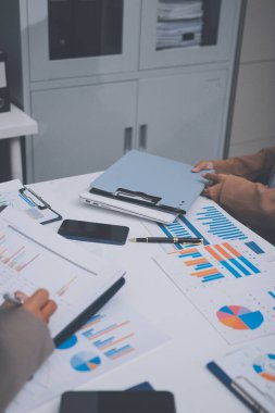 İş arkadaşları, modern bir ofis ortamında yapılan önemli bir toplantıda strateji ve piyasa performansı hakkında tartışırken finansal tablolar ve raporları analiz ediyorlar.