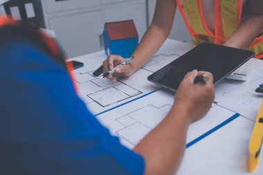 Mühendis ve mimar, hareketli bir şantiyede planlar ve inşaat planlarını birlikte gözden geçiriyorlar.