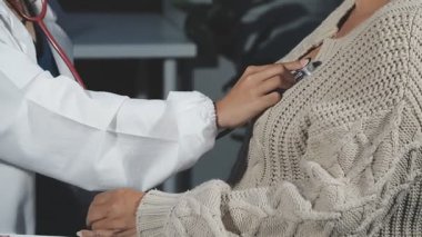 Üniformalı genç bayan doktor steteskop tutuyor ve gülümsüyor. Hasta resepsiyonda oturuyor. Steteskoplu doktor.