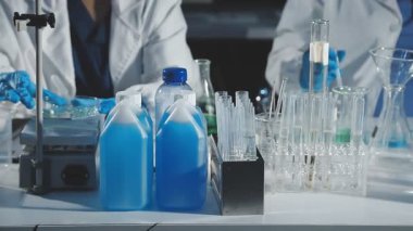 Koruyucu eldivenler ve eldivenler giyen bilim adamı kimya laboratuarında pipetli matara tutuyor.