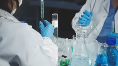 Koruyucu maskeli bir laboratuvar çalışanı elinde bir tüp tutuyor ve deneyler yapıyor.