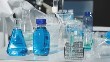 Mavi üniformalı bir laboratuvar asistanı ve cam şişede sıvı bulunan bir tıbbi maske..