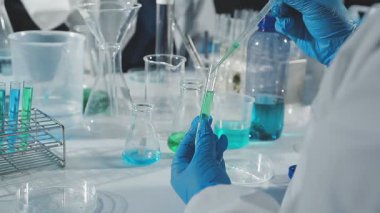 Mavi eldivenli laboratuvar asistanı ve koruyucu maskeli cam tüplü kimyasal laboratuvar sıvısı.