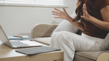 Genç bir kadın oturma odasında oturuyor ve dizüstü bilgisayar kullanıyor.