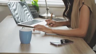 Ofisteki masada dizüstü bilgisayar ve akıllı telefonla çalışan bir iş kadını.