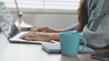 Genç Asyalı adam dizüstü bilgisayar kullanıyor ve sabahları çay içiyor.