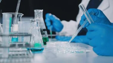 Yakın çekim. Mavi ceketli laboratuvar asistanı elinde sıvı ve pipetle duruyor..