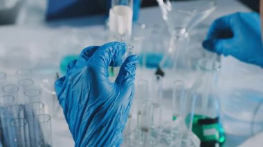 Koruyucu eldivenli laboratuvar teknisyeni elinde sıvı test tüpleri tutuyor.