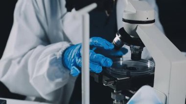 Koruyucu üniformalı bilim adamı bir laboratuarda mikroskop tutuyor..