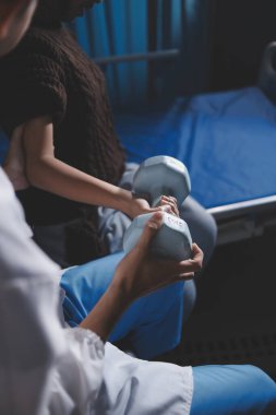 Evde dambıl kullanarak fizyoterapist eğitimi alan yaşlı bir kadın. Terapist, huzurevi egzersizlerinde yaşlı kadına yardım ediyor. Yaşlı bir hasta kollarını uzatmış halterler kullanıyor..