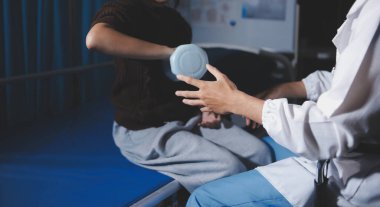 Evde dambıl kullanarak fizyoterapist eğitimi alan yaşlı bir kadın. Terapist, huzurevi egzersizlerinde yaşlı kadına yardım ediyor. Yaşlı bir hasta kollarını uzatmış halterler kullanıyor..