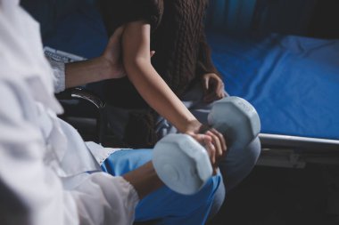 Evde dambıl kullanarak fizyoterapist eğitimi alan yaşlı bir kadın. Terapist, huzurevi egzersizlerinde yaşlı kadına yardım ediyor. Yaşlı bir hasta kollarını uzatmış halterler kullanıyor..