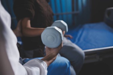 Evde dambıl kullanarak fizyoterapist eğitimi alan yaşlı bir kadın. Terapist, huzurevi egzersizlerinde yaşlı kadına yardım ediyor. Yaşlı bir hasta kollarını uzatmış halterler kullanıyor..