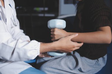 Evde dambıl kullanarak fizyoterapist eğitimi alan yaşlı bir kadın. Terapist, huzurevi egzersizlerinde yaşlı kadına yardım ediyor. Yaşlı bir hasta kollarını uzatmış halterler kullanıyor..