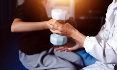 Evde dambıl kullanarak fizyoterapist eğitimi alan yaşlı bir kadın. Terapist, huzurevi egzersizlerinde yaşlı kadına yardım ediyor. Yaşlı bir hasta kollarını uzatmış halterler kullanıyor..