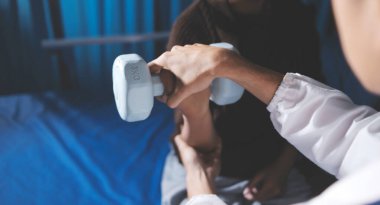 Evde dambıl kullanarak fizyoterapist eğitimi alan yaşlı bir kadın. Terapist, huzurevi egzersizlerinde yaşlı kadına yardım ediyor. Yaşlı bir hasta kollarını uzatmış halterler kullanıyor..